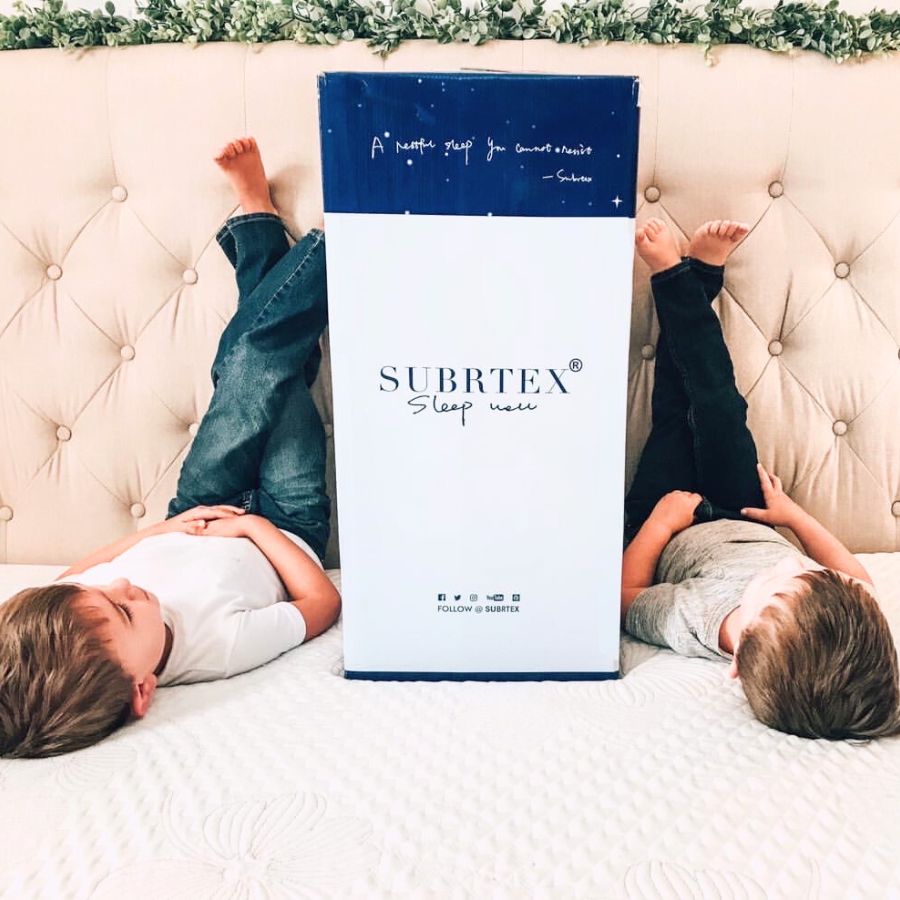 Two kids lying next to Subrtex mattress topper packaging